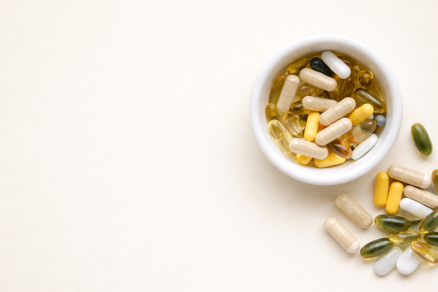 Natural vitamins and supplements capsules in ceramic bowl on neutral background
